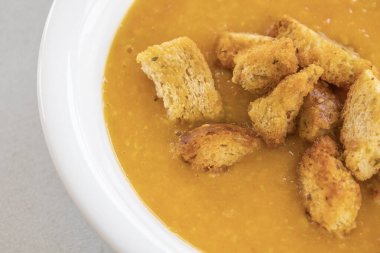 Kremalı domates ve kabak çorbası beyaz bir kasede servis edilir, üzerinde ev yapımı kızarmış ekmek vardır.