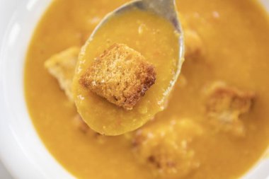 Kremalı domates ve kabak çorbası beyaz bir kasede servis edilir, üzerinde ev yapımı kızarmış ekmek vardır.