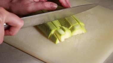 Parlak bir mutfakta beyaz bir kesme tahtasıyla taze kabak doğrayan bir kadının yakın çekim videosu.
