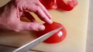 Kadınların elleri olgun domatesleri beyaz bir kesme tahtasıyla kesiyor.