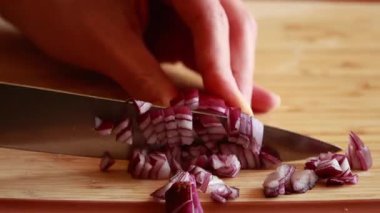 Ahşap kesme tahtasının üzerinde kırmızı soğan doğrayan ellerin yakın çekim videosu.