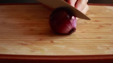 Ahşap kesme tahtasının üzerinde kırmızı soğan doğrayan ellerin yakın çekim videosu.