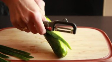 Bir kadının elleriyle ahşap kesme tahtasındaki salatalığı soyarken çekilmiş yakın çekim videosu.