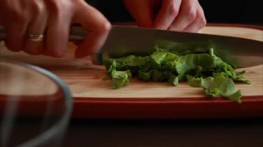 Kadının ellerinin tahta kesme tahtasındaki taze marulu dilimlediği yakın çekim video.