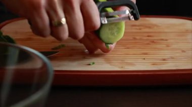 Bir kadının elleriyle ahşap kesme tahtasındaki salatalığı soyarken çekilmiş yakın çekim videosu.