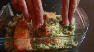 Kadın elinin somon filetosunu ekmek kırıntılarıyla kapladığı yakın çekim videosu. Filetolar eşit şekilde bastırılıp, pişirilmeye hazırlanıyor.