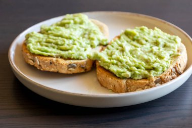 Üzerine kremalı avokado sosu serpiştirilmiş iki dilim kızarmış ekmek. Basit ve sağlıklı bir kahvaltı. 