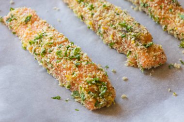 Çiğ somon fileto yakın çekim bir tepside dizilmiş, pişirilmeye hazır. Somon, ekmek kırıntılarıyla eşit kaplıdır. Doku ve tazeliği gösterir.