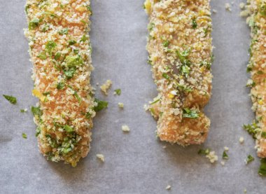 Çiğ somon fileto yakın çekim bir tepside dizilmiş, pişirilmeye hazır. Somon, ekmek kırıntılarıyla eşit kaplıdır. Doku ve tazeliği gösterir.