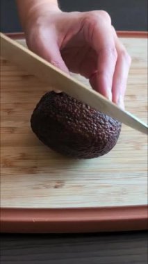 Bir kadının elleri, olgun bir avokadoyu tahta kesme tahtasıyla keserken yakın çekim videosu.