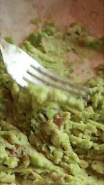  Kremalı avokado püresi yapmak için çatal kullanarak bir kâsede olgun avokadoyu ezmek.