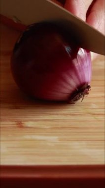 Tahta kesme tahtasıyla kırmızı soğan doğrayan bir kadının elleri.
