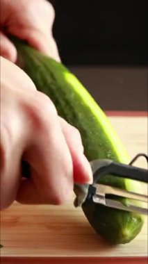 Bir kadının elleriyle ahşap kesme tahtasındaki salatalığı soyarken çekilmiş yakın çekim videosu.