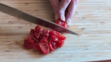 Bir kadın elinin tahta kesme tahtasıyla taze domatesleri doğradığı yakın çekim videosu.