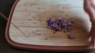 Bir kadının ellerinin tahta kesme tahtasındaki kırmızı soğanı dilimleyip doğradığı yakın çekim videosu.