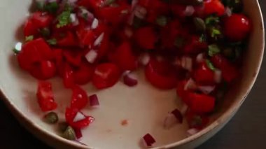 Çeri domatesler, kırmızı soğan, kapari ve maydanozdan yapılmış taze salsa sosu kasede servis edilir.