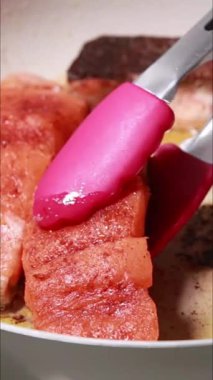 Tavada tereyağı banyosunda pişen taze somon filetolarının dikey yakın çekim videosu.