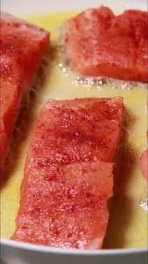 Tavada tereyağı banyosunda pişen taze somon filetolarının dikey yakın çekim videosu.