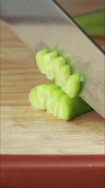 Dikey yakın çekim videoda bir kadının elleri ahşap bir tahtanın üzerinde soyulmuş bir salatalığı kesiyor.