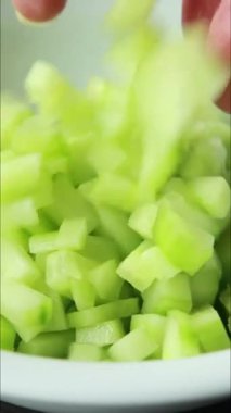 Dikey yakın çekim videoda bir kadının elleri ahşap bir tahtanın üzerinde soyulmuş bir salatalığı kesiyor.