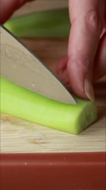 Dikey yakın çekim videoda bir kadının elleri ahşap bir tahtanın üzerinde soyulmuş bir salatalığı kesiyor.