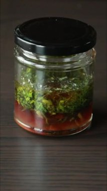 Yeşil taze otlarla dolu bir kavanozda lezzetli bir salata sosu hazırlama sürecini gösteren yakın çekim videosu.