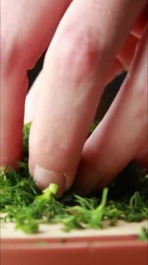 Tahta bir tahtada taze dereotu kesen bir bıçağı gösteren dikey yakın plan bir video. Yeşil bitki ince ince dilimlenmiş, hızlı ve temiz kesikler.