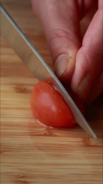 Bir kadının elleri, tahta bir kesme tahtasıyla kiraz domateslerini dilimliyor.