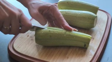 Kadının elleri, tahta bir kesme tahtasıyla taze kabağı ikiye bölüyor.