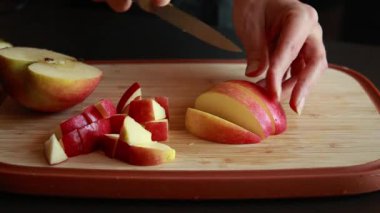 Kadınların elleri, taze bir elmayı tahta bir kesme tahtasıyla kesiyor.