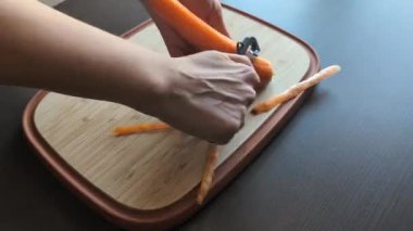  Kadınların elleri taze havucu soyarken tahta kesme tahtasına.