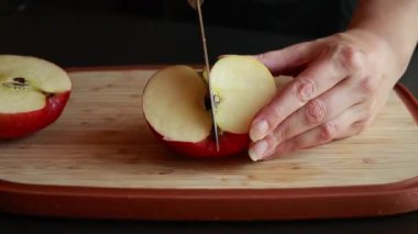 Kadınların elleri, taze bir elmayı tahta bir kesme tahtasıyla kesiyor.