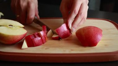 Kadınların elleri, taze bir elmayı tahta bir kesme tahtasıyla kesiyor.