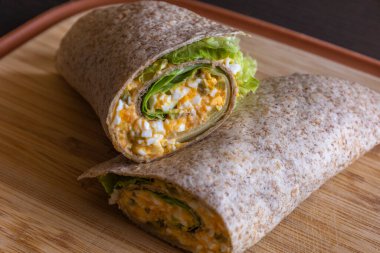 Şeytan yumurtası sağlıklı kahvaltıyı tahta kesme tahtasına sarar. Taze, hafif bir yemeğin yakın plan fotoğrafı. Güzelce paketlenmiş kremalı şeytan yumurtaları. Güne sağlıklı başlamak için ideal.