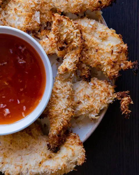 Hindistancevizi parçalarıyla kaplı tavuk filetolarının yakın plan fotoğrafı, acı biber soslu bir tabağa konmuş. Tropikal lezzet yemeği, gevrek dokular, zengin bir tat.