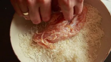 Kadınların elleri çiğ tavuk filetolarını hindistan cevizi parçacıklarıyla kaplıyor. Basit ve temiz yemek hazırlığı