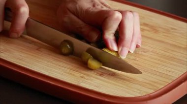 Kadın elleri tahta kesme tahtasının üzerinde turşu dilimliyor ve doğruyor.