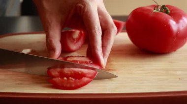 Kadının elleri, büyük sulu bir domatesi tahta kesme tahtasıyla kesiyor.