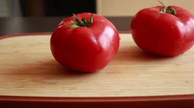 Kadının elleri, büyük sulu bir domatesi tahta kesme tahtasıyla kesiyor.