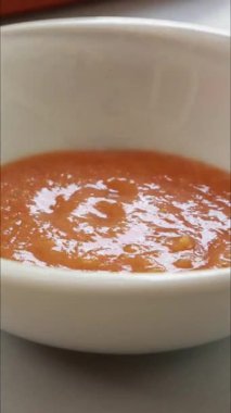 Bir kasede sıcak domates ve kabak çorbası servis eden ve üstüne ev yapımı kızarmış ekmek koyan ellerin yakın plan görüntülerini gösteren dikey bir video.