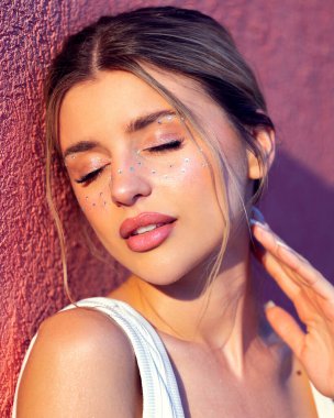 Pembe pullu, kalın makyajlı bir kadın. Güneş ışığına yakalanmış. Sanatsal ve şenlikli görünüş, festival, güzellik, moda veya yaz temalı hisse içeriği için mükemmel