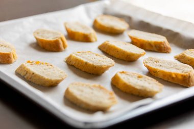  Bir tepside düzgünce dizilmiş ekmek dilimleri, crostini içinde pişirilmeye hazır.