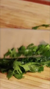 Kadın maydanozu tahta kesme tahtasıyla kesiyor. Dikey videoyu kapat.