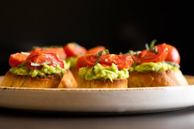 Kavrulmuş kiraz domatesli avokado crostini ve taze fesleğen. Isırık büyüklüğünde bir parti aperatifi olarak servis ediliyor. Yemek blogları ve eğlenceli fikirler için mükemmel.