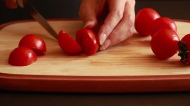 Bir kadının elleri tahta kesme tahtasındaki taze domatesleri dilimlerken çekilmiş yakın çekim videosu.