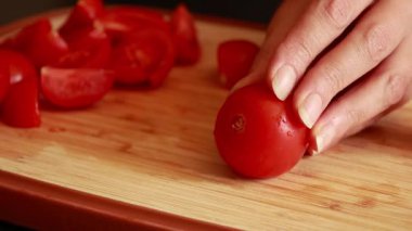 Bir kadının elleri tahta kesme tahtasındaki taze domatesleri dilimlerken çekilmiş yakın çekim videosu.