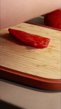 Kadın elleri kırmızı dolmalık biber dilimleyip dikey mutfak videosu hazırlıyor.