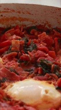 Yumurta ve domatesli geleneksel shakshuka dikey çekim pişiriyor.