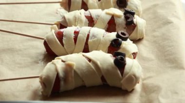 Çiğ Cadılar Bayramı mezeleri sosise sarılmış ve zeytinlerle süslenmiş sosislerden yapılmış mumyalar. Cadılar Bayramı partisi için pişirilmeye hazır ürkünç abur cubur fikri.