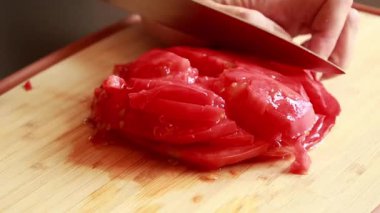 Kadınların elleri, tahta kesme tahtasında sulu bir domatesi kesiyor.